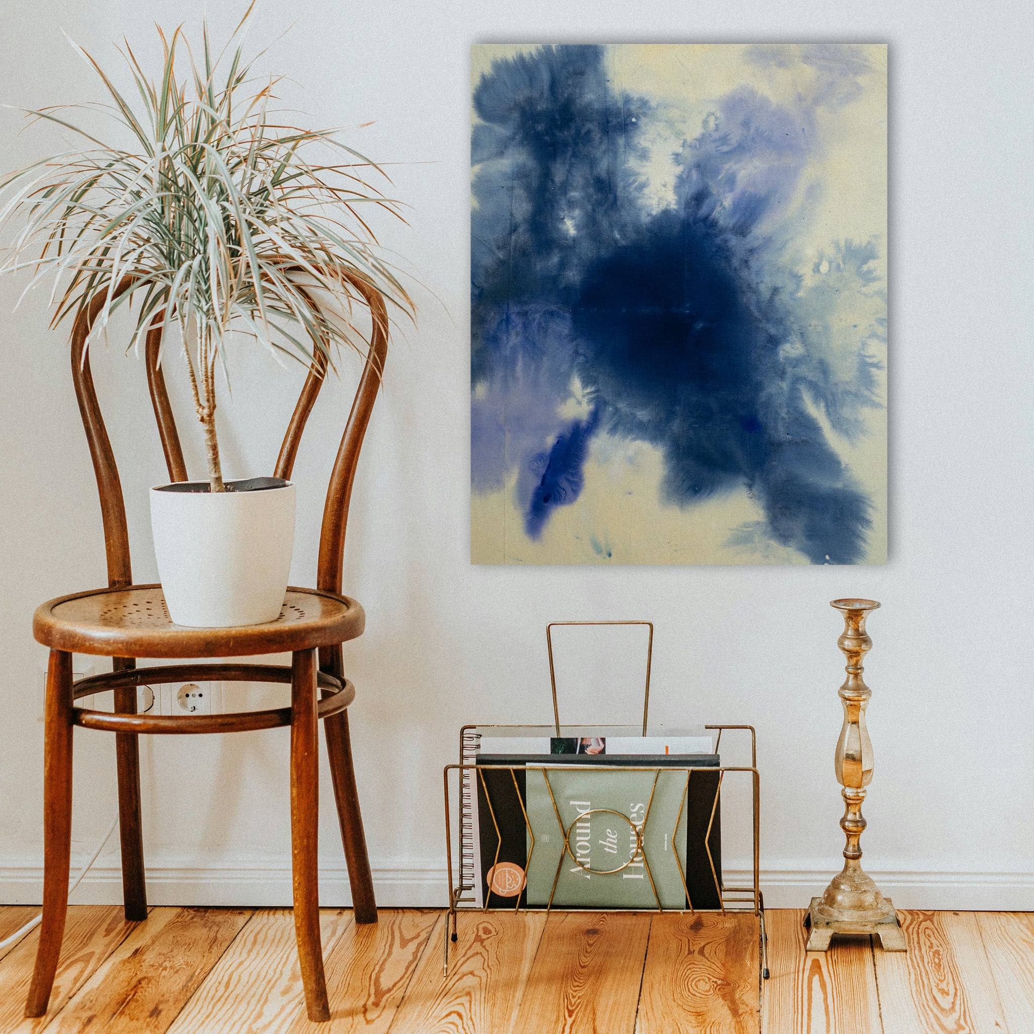 A blue abstract painting on an off-white background hangs above a magazine rack and next to a cafe chair
