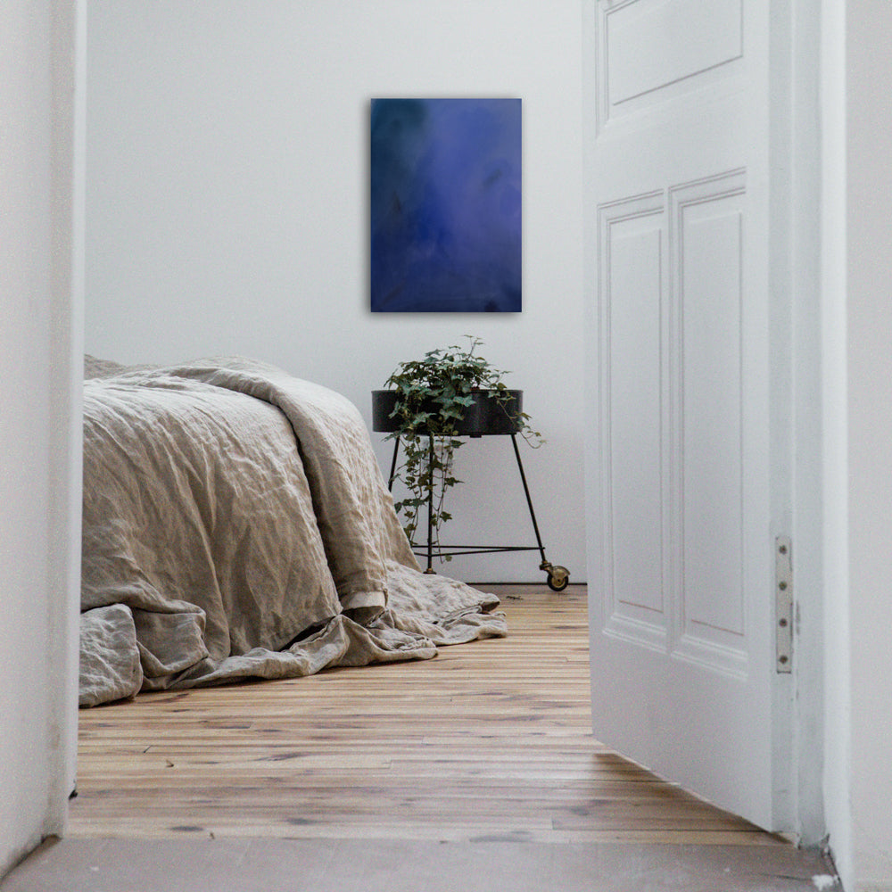 A cool blue abstract painting hangs above a plant in a bedroom
