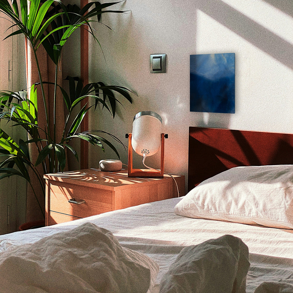 A blue abstract painting hangs above an unmade bed in a sunny room