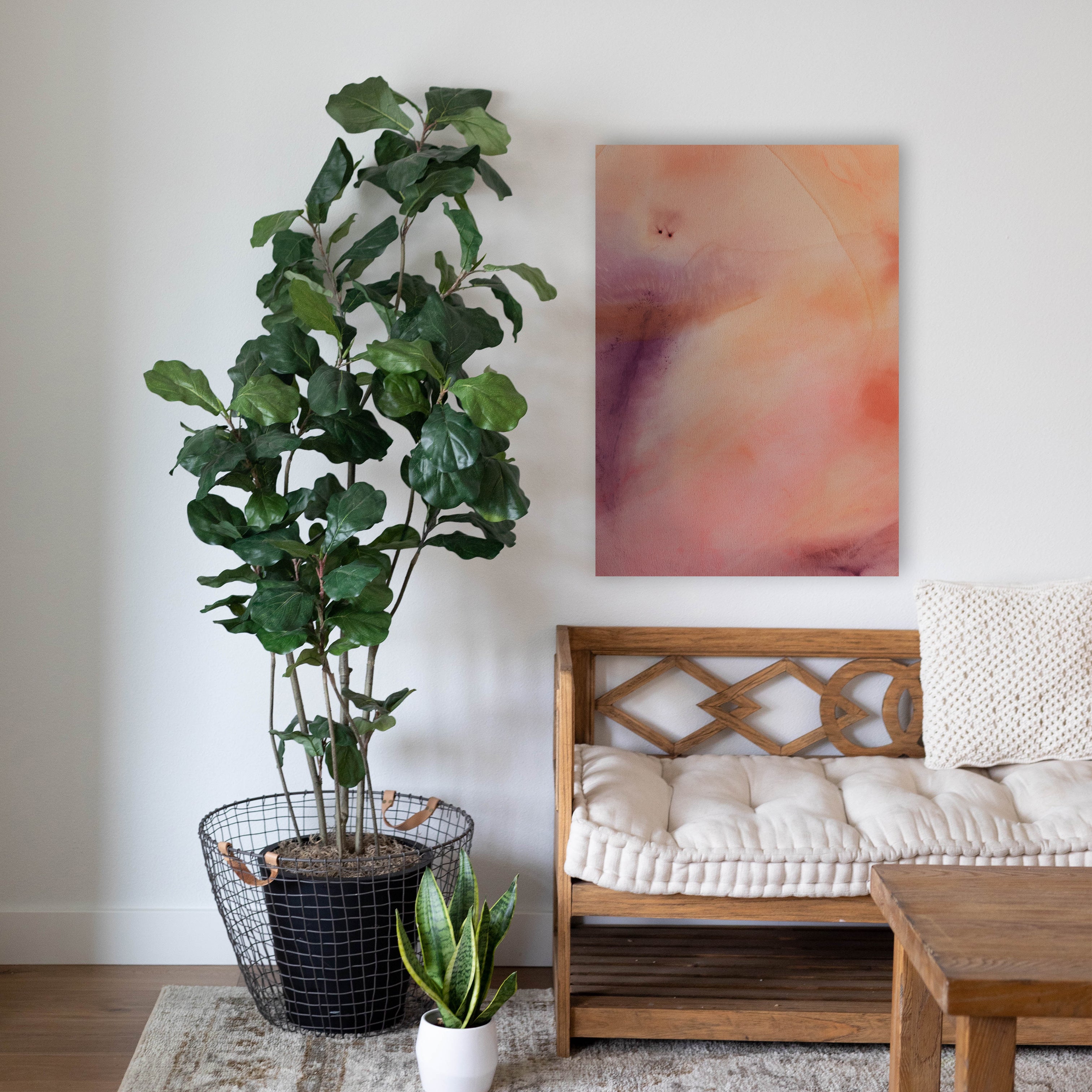 Purple, pink, and orange abstract painting hangs above a wooden bench, next to a large green plant.